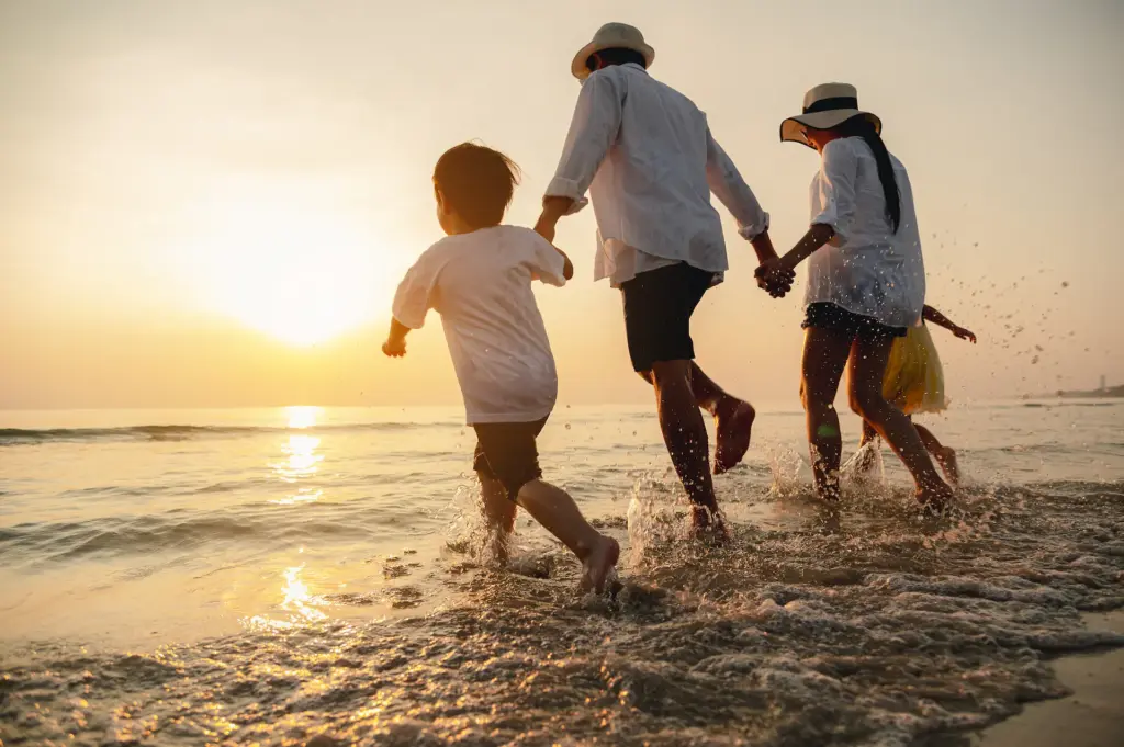 Family running through ocean waves at sunset