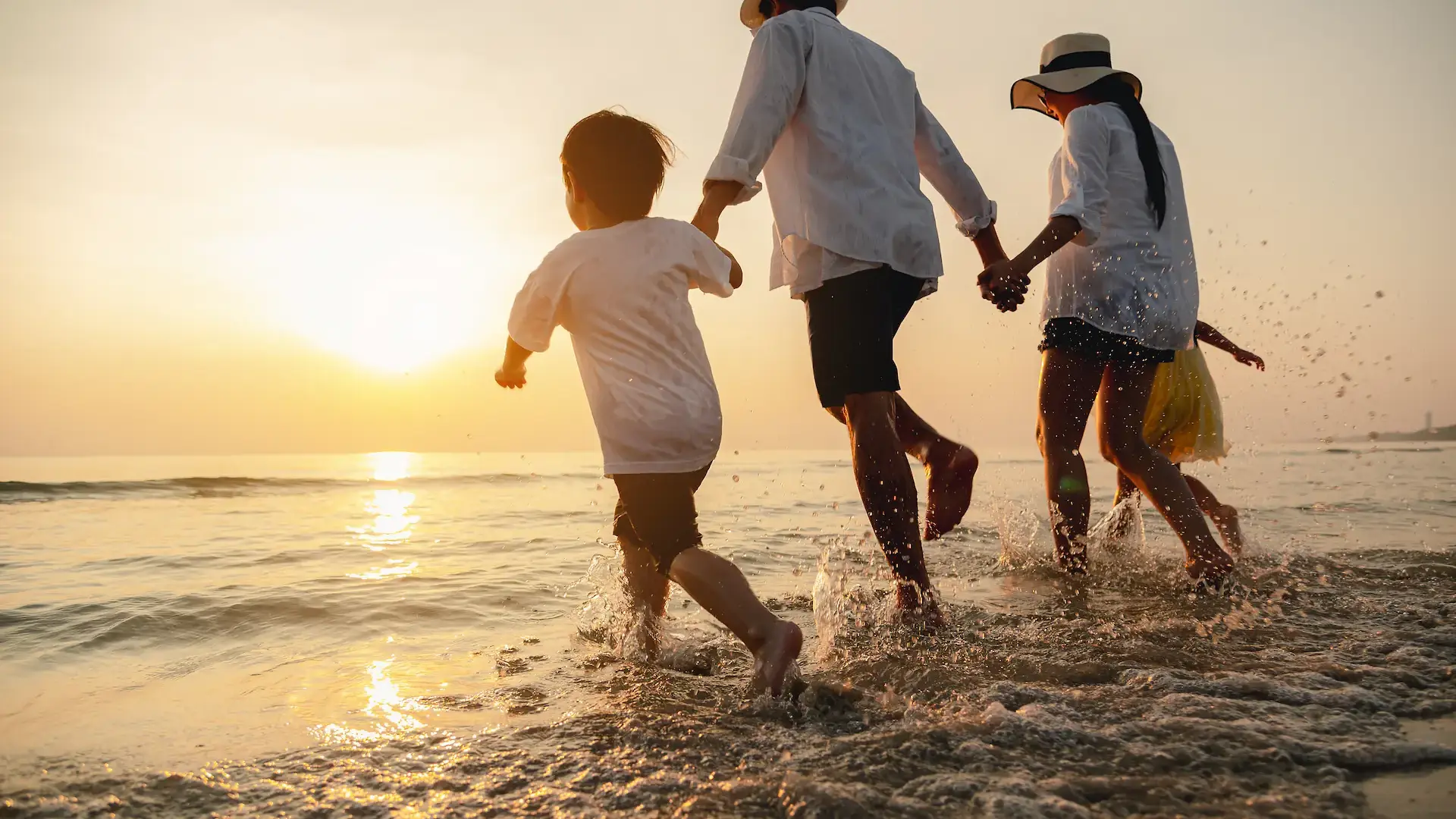 Family running through ocean waves at sunset