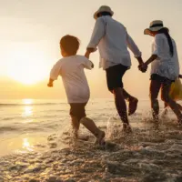 Family running through ocean waves at sunset