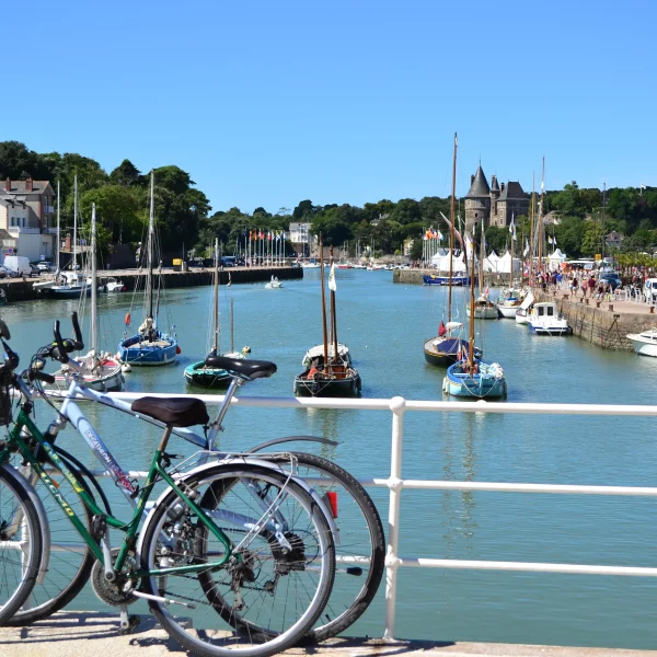 Vélos devant port avec voiliers et maisons côtières