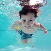 Enfant souriant nage sous l’eau en piscine