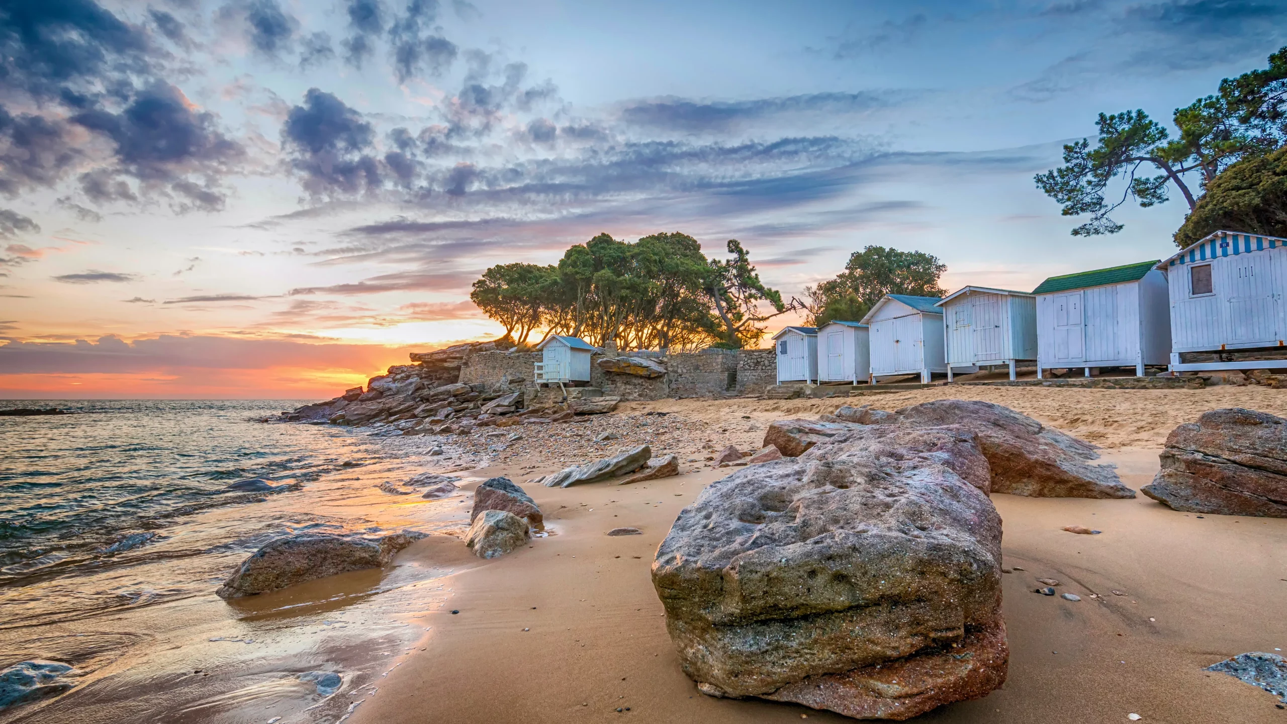 Cabanes blanches sur plage rocheuse au coucher du soleil