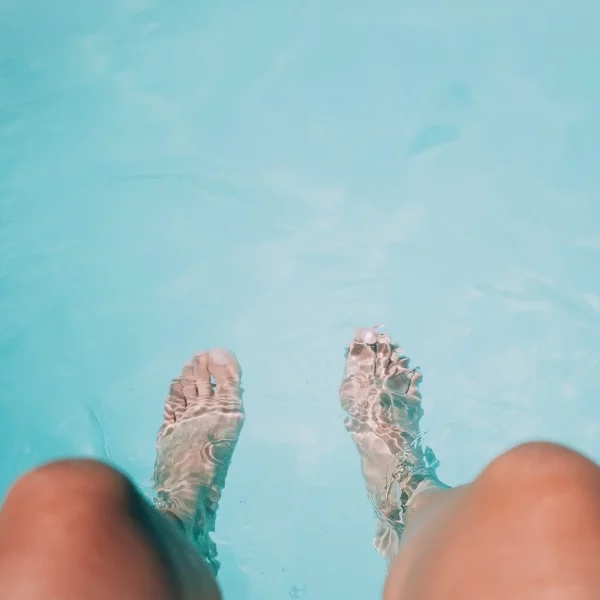 Pieds immergés dans une piscine turquoise claire