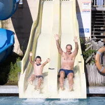 Père et fils dévalant toboggan aquatique bras levés