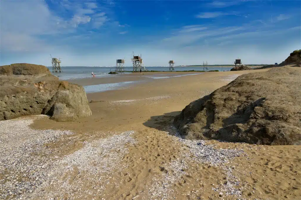 Plage sableuse avec carrelets et rochers au premier plan