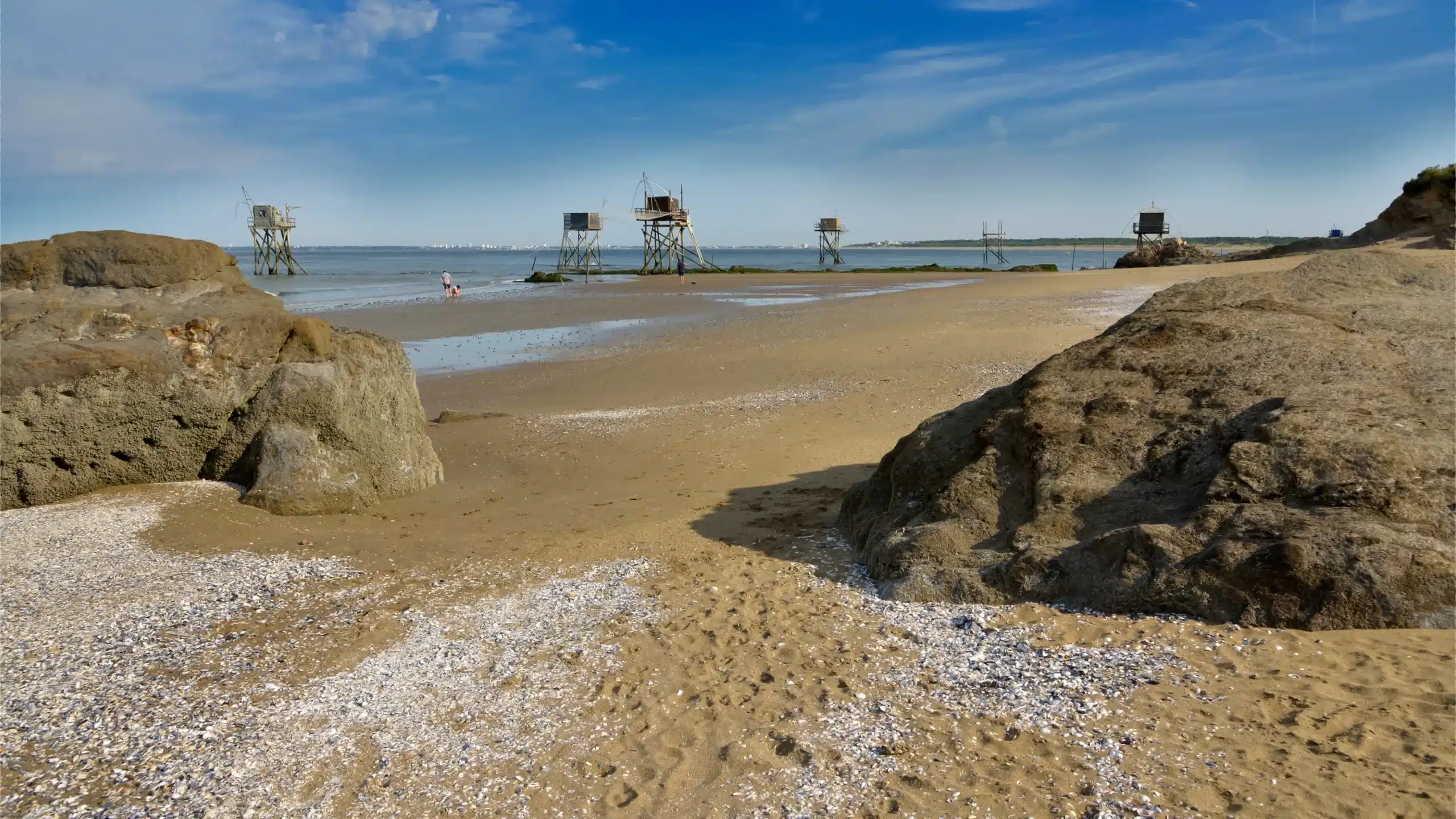 Plage sableuse avec carrelets et rochers au premier plan