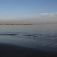 Plage calme avec jetée et phare au loin