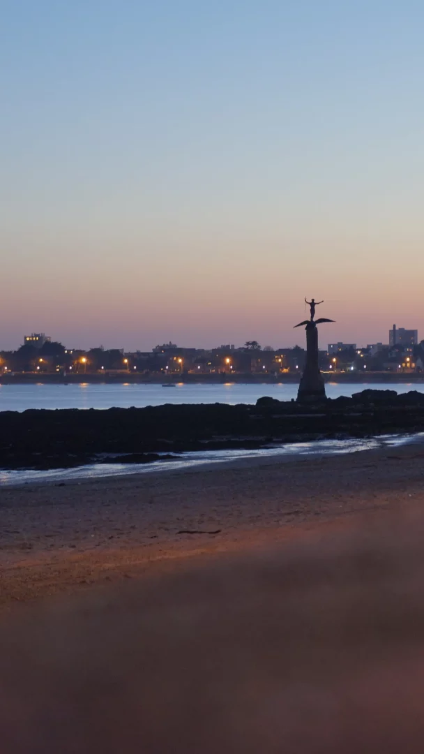Plage au crépuscule avec statue et ville illuminée